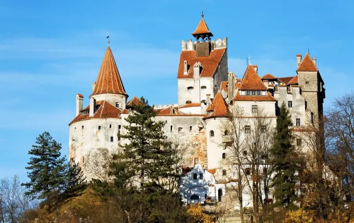 Transilvanya’da kayalık bir tepe üzerinde yükselen, turuncu çatılı ve gotik kuleleriyle ünlü Bran Şatosu’nun güneşli bir günde çekilmiş fotoğrafı.